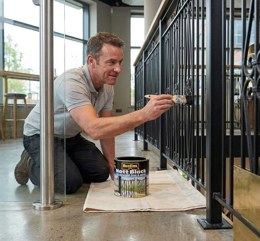 Man painting a black metal railing inside a building with Rust-Oleum paint can.